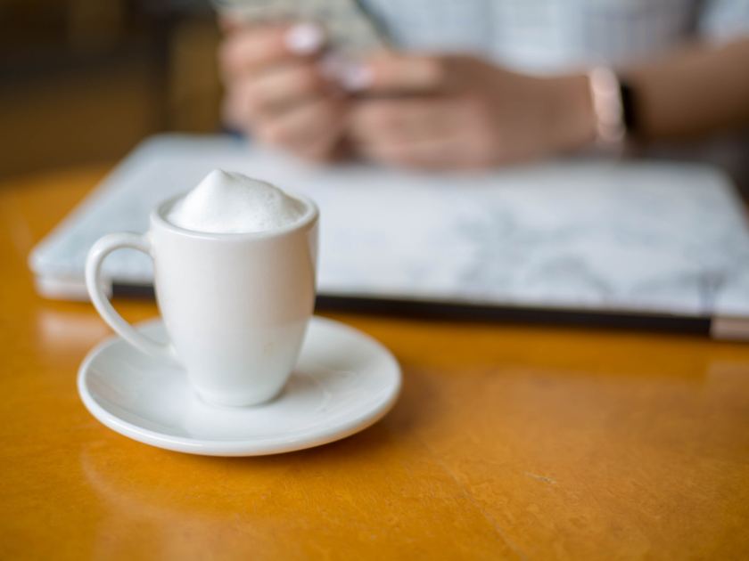 A coffee and a tablet on a desk, someone working just out of frame