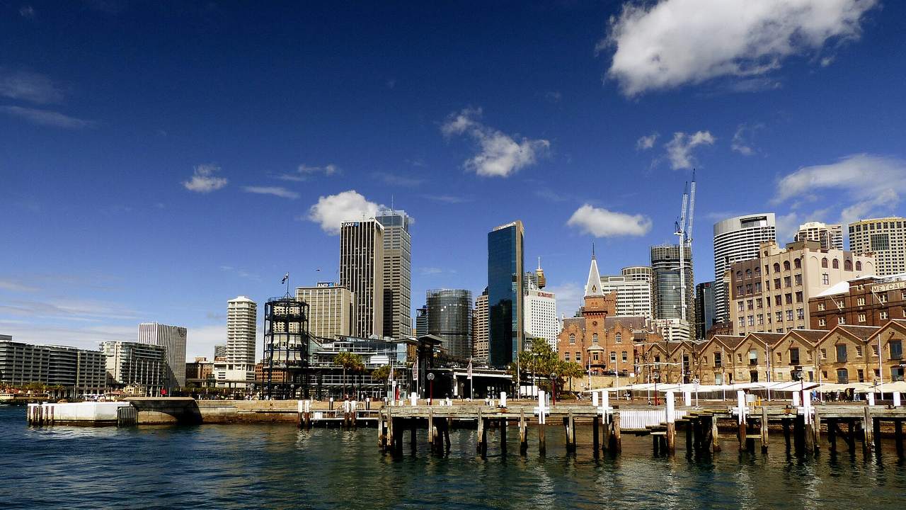 Sydney seen across the water from The Rocks: the sandstone stores and a timber wharf at Campbell’s Cove, with the city towers behind them