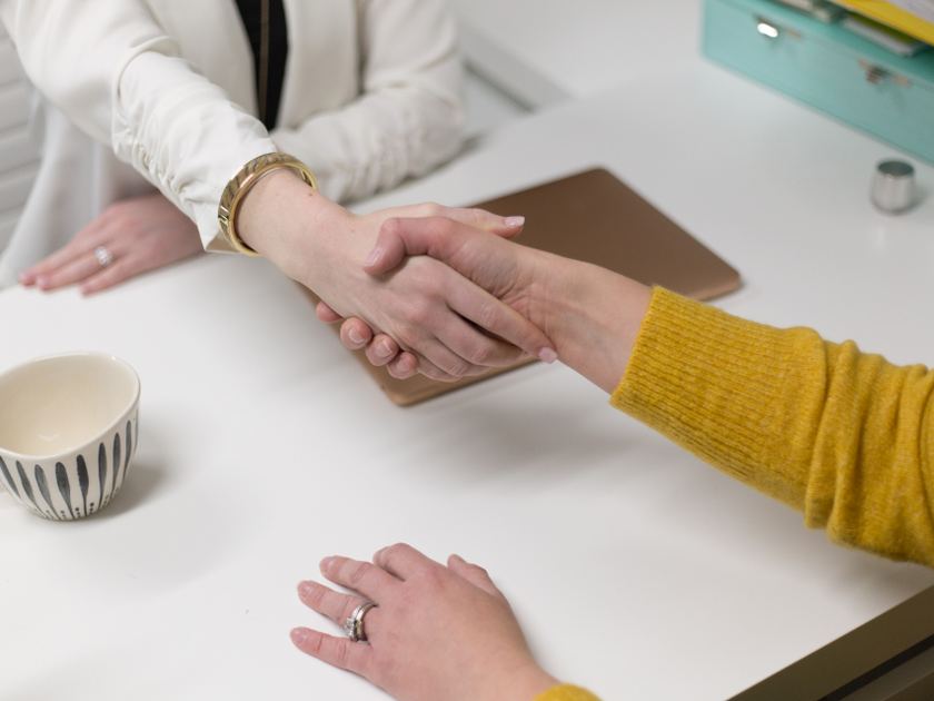Two people shaking hands across a table, seen from the side, faces out of frame