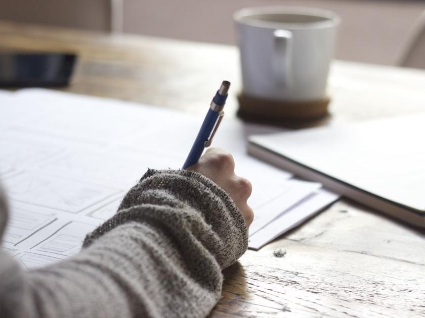 A hand writing on a clipboard beside a mug at a light table